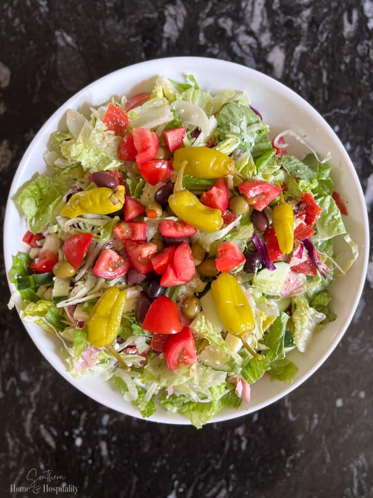 Tomatoes, pepperoncini peppers, and olives topping Italian salad