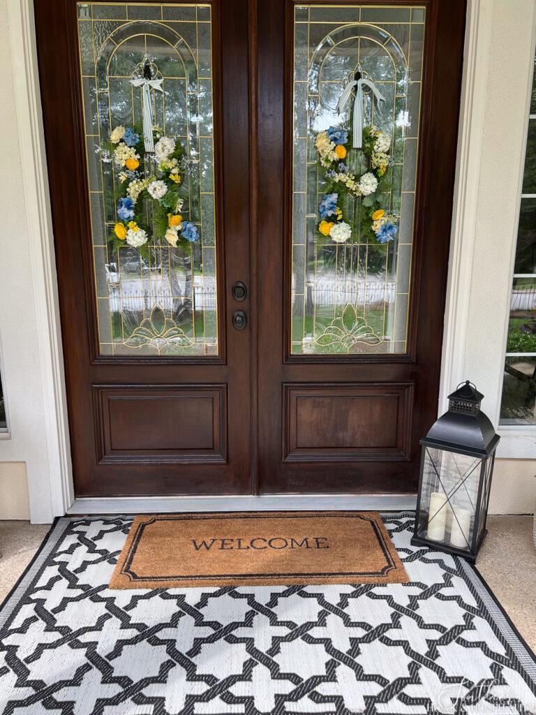 Layering black and white rug on front porch with welcome mat