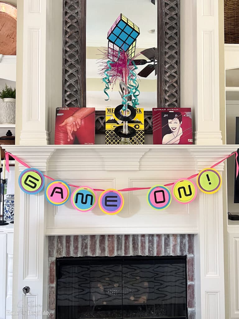 Pennant letter banner and rubik's cube centerpiece on fireplace mantel for 80's party