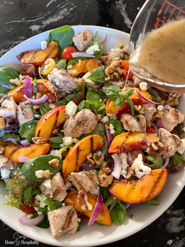 Pouring balsamic vinaigrette dressing on grilled chicken and peach salad
