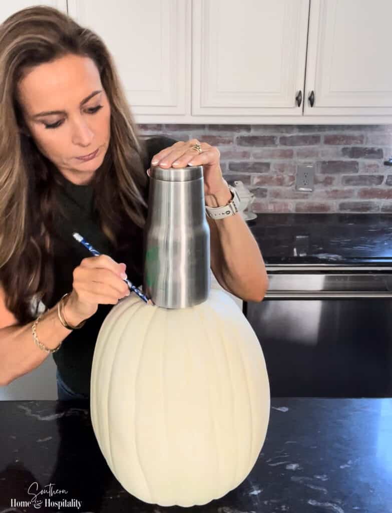 Drawing an outline on carvable pumpkin to make a fall vase