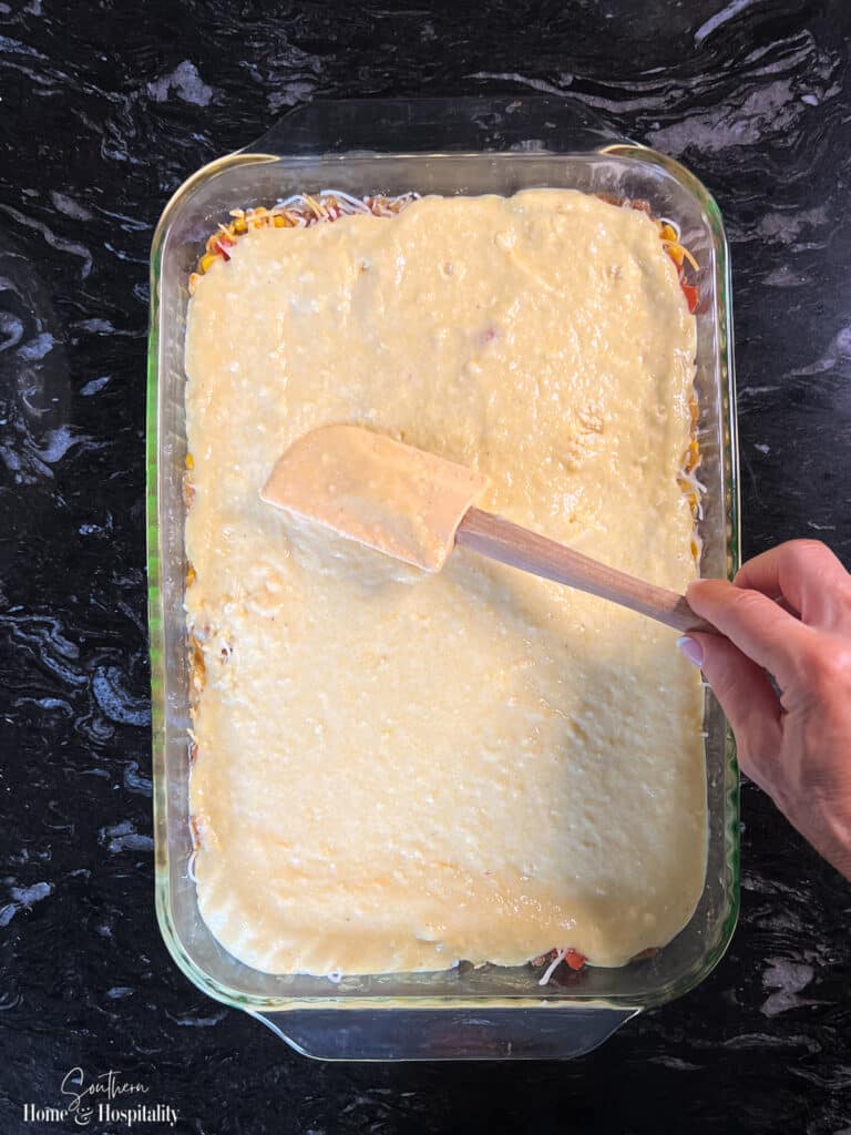 Spreading cornbread batter over meat mixture for mexican casserole