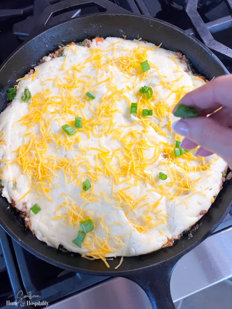 sprinkling cheese on top of shepherd's pie mashed potatoes
