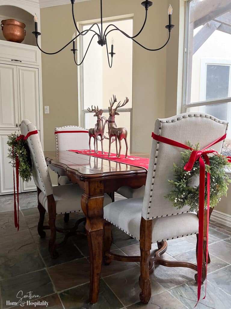Christmas wreaths hanging on back of upholstered dining chairs