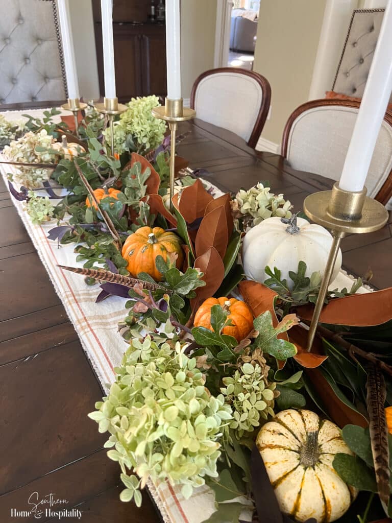 Natural fall dining table centerpiece with pumpkins, foraged leaves, and hydrangeas