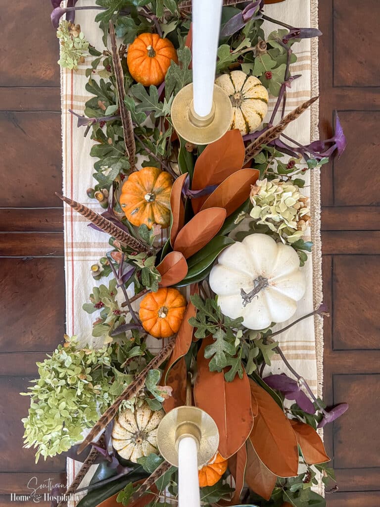 Fall centerpiece with orange and white pumpkins, magnolia leaves, and feathers