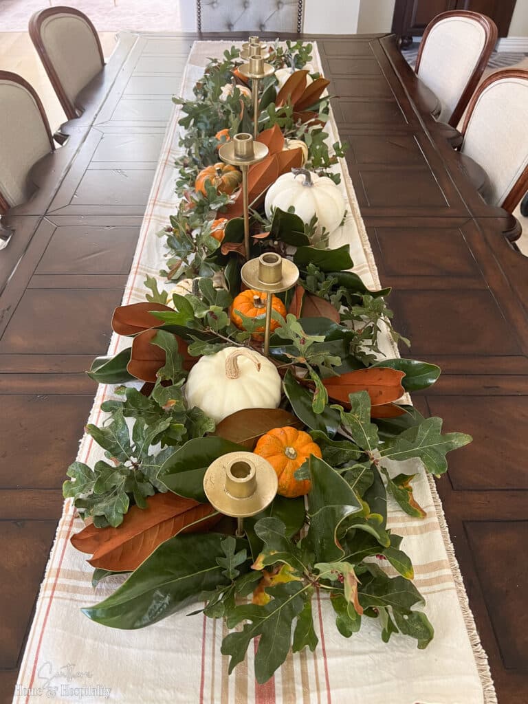 Fresh magnolia branches arranged with pumpkins and brass candlesticks on a fall table
