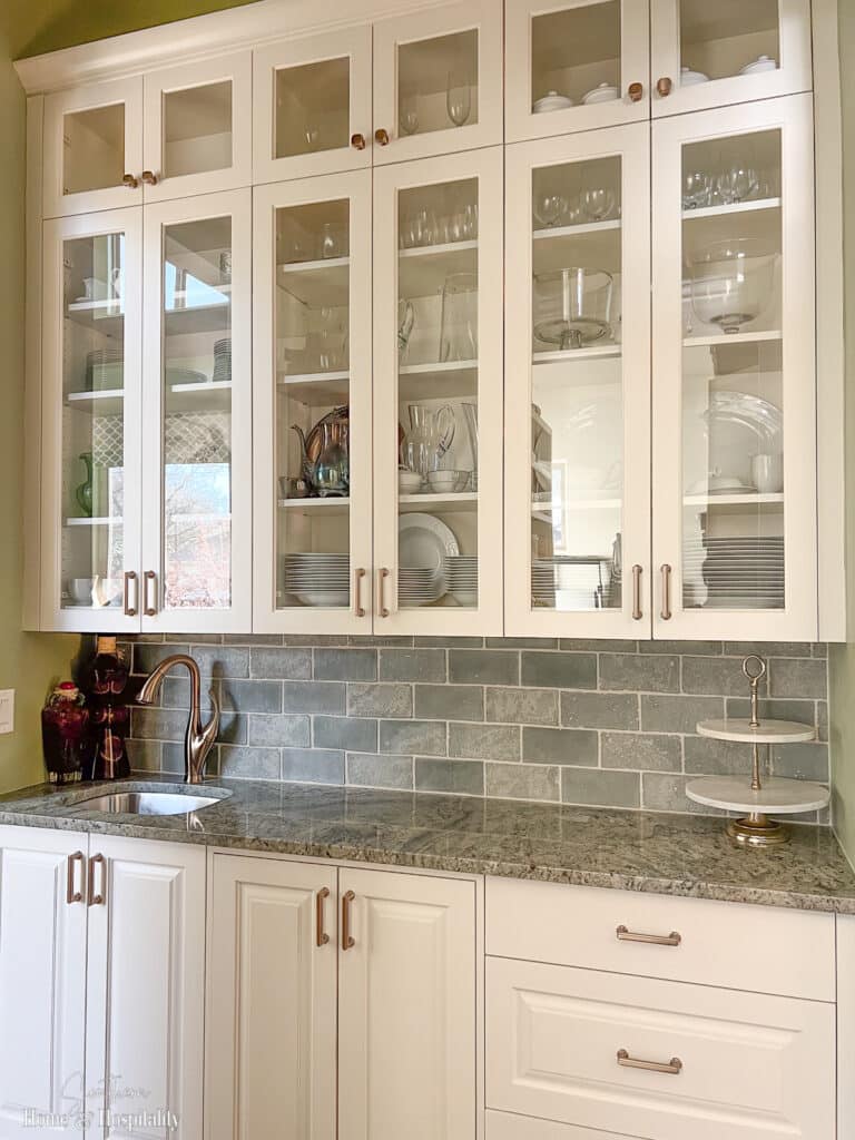 Butler's pantry with white cabinets, glass front doors, and champagne hardware