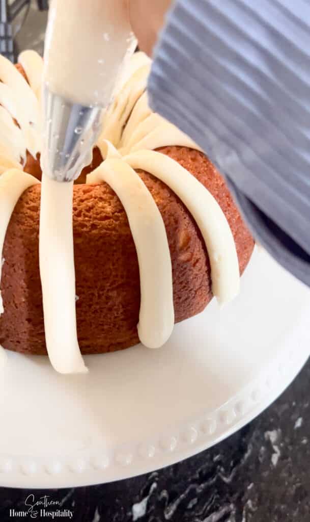 Piping stripes of cream cheese icing onto a bundt cake
