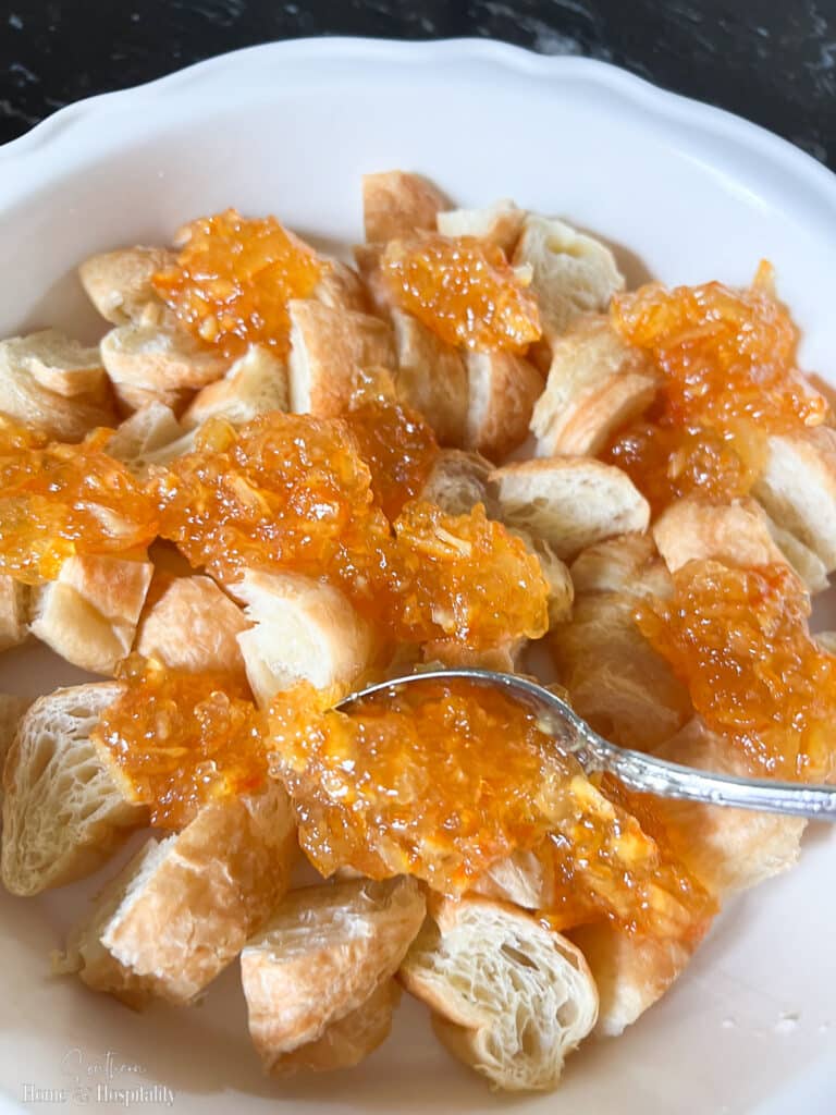 Spooning orange marmalade on croissants for breakfast casserole