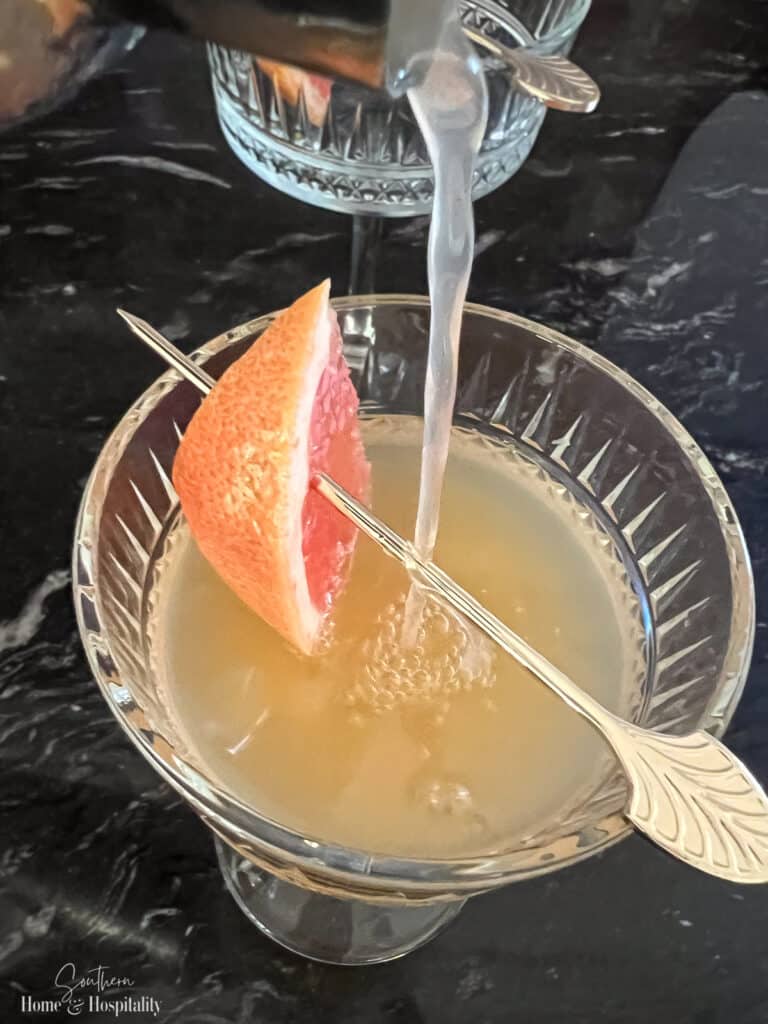 Pouring French Blonde drink into glass with grapefruit garnish
