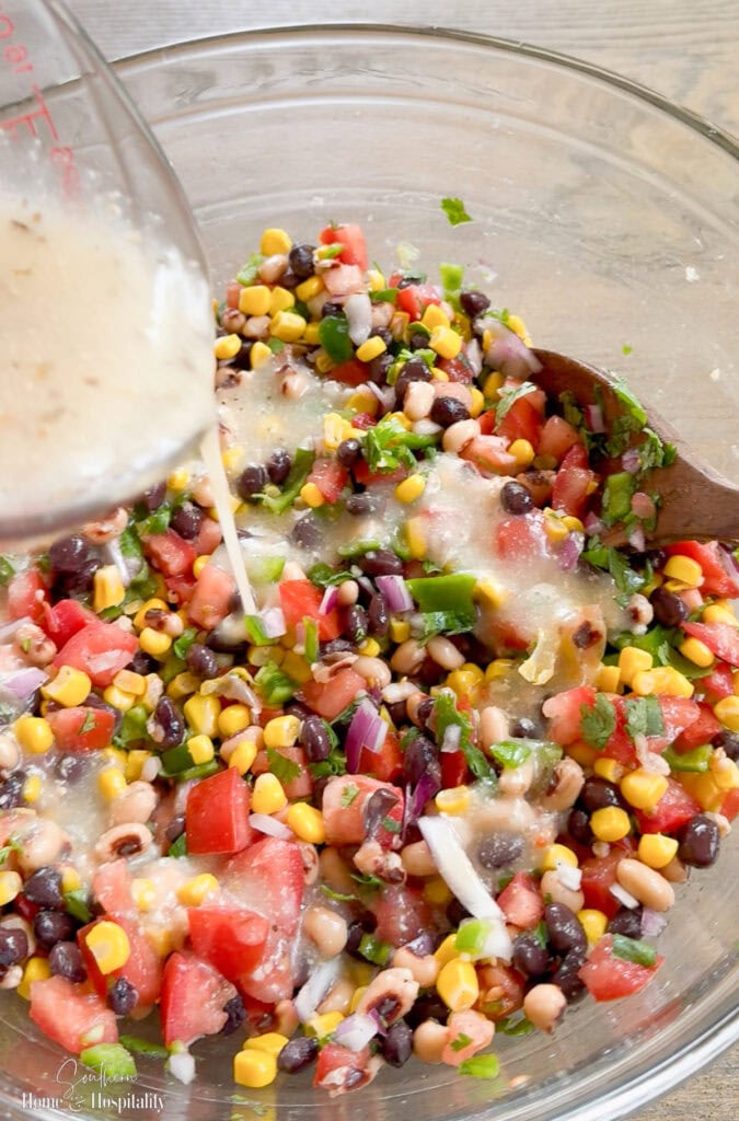 Bottled Italian dressing being poured over a bowl of cowboy caviar ingredients.