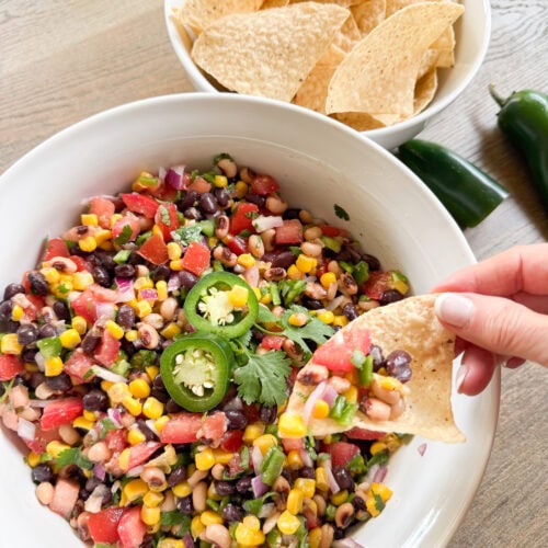 A colorful bowl of cowboy caviar made with beans, corn, bell peppers, tomatoes, and Italian dressing, served with tortilla chips.