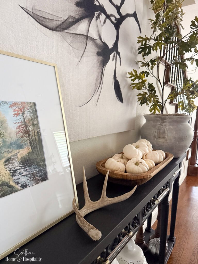Fall console table with wicker, wood, antler, and muted green branches.