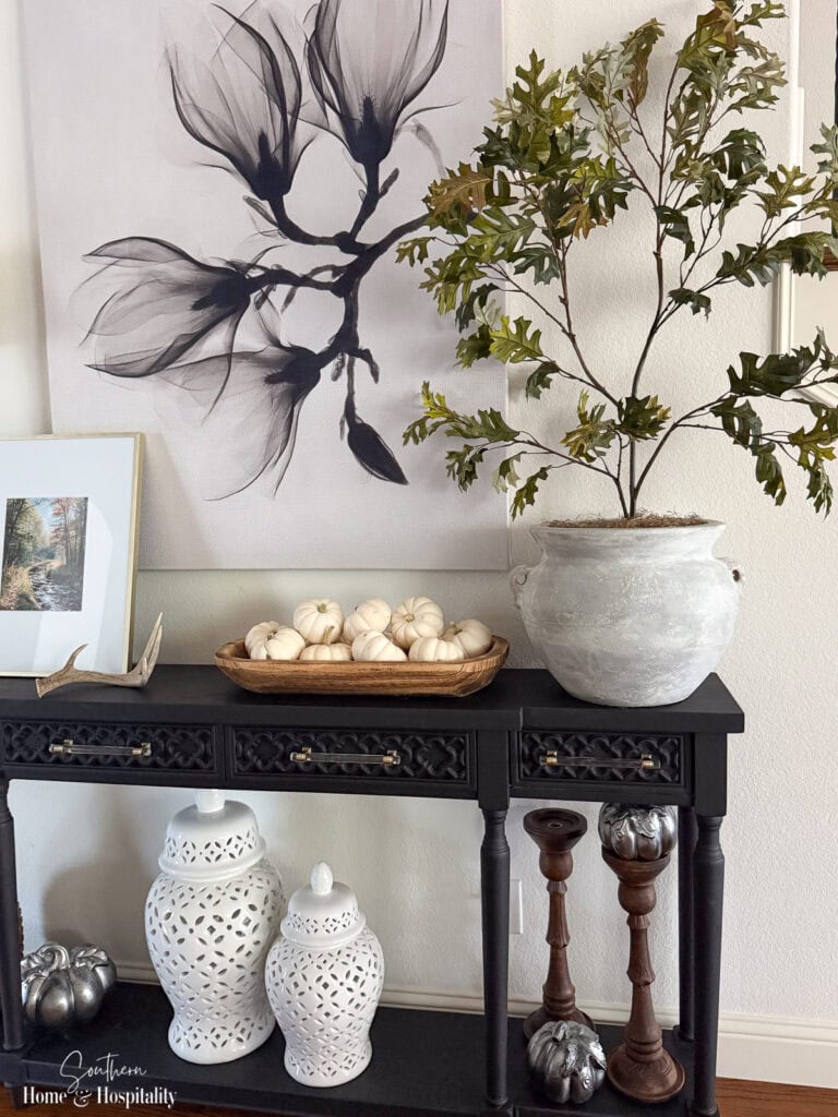 Narrow console table styled with fall decor in earthy tones and muted green.