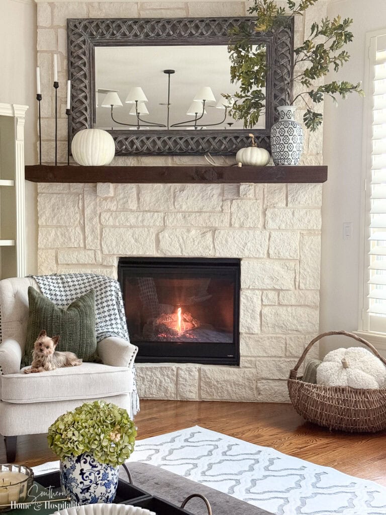 Elegant fall living room with subdued green and blue accents and dog relaxing in chair by the fireplace.