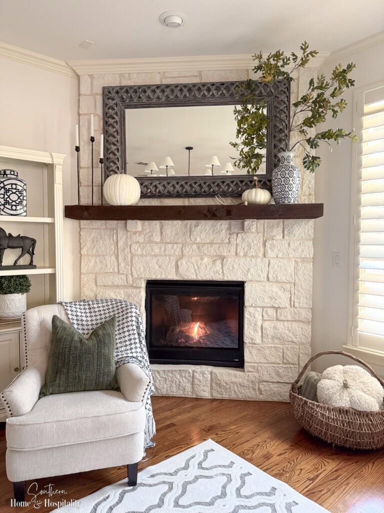 Fall mantel with muted green branches, white pumpkins, and black candlesticks.