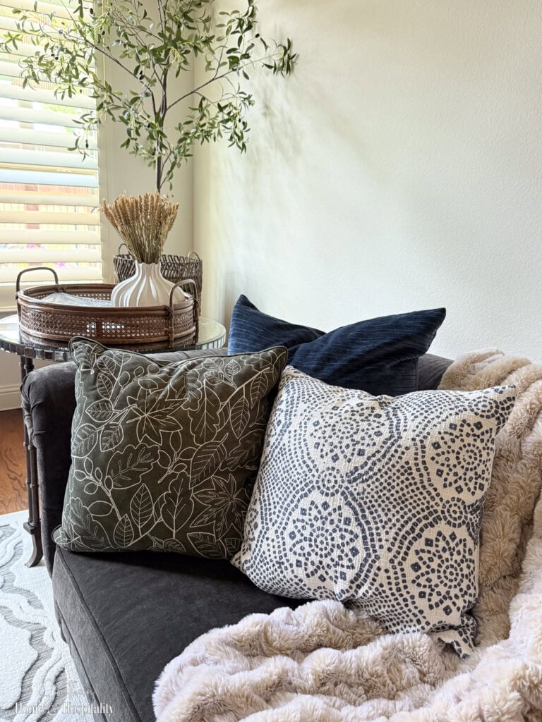 Cozy fall sofa with olive green velvet and midnight blue velvet pillows and a faux fur throw.