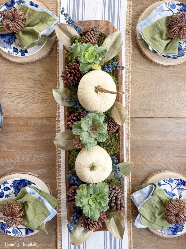 Overhead shot of blue and green fall centerpiece styled with faux blueberries, moss, and ornamental cabbage.