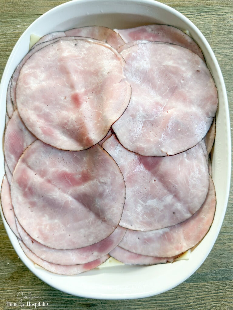 Thinly sliced deli ham layered over cheese on Hawaiian rolls for hot ham and cheese sliders.
