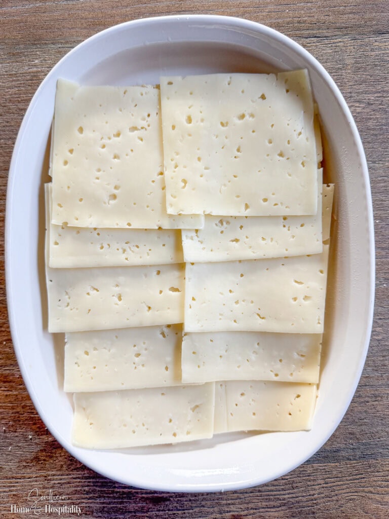 First layer of Swiss cheese added to Hawaiian rolls in baking dish for baked ham and cheese sliders.