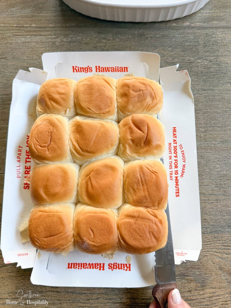 Sheet of Hawaiian rolls sliced horizontally with a serrated knife to make ham and cheese sliders.