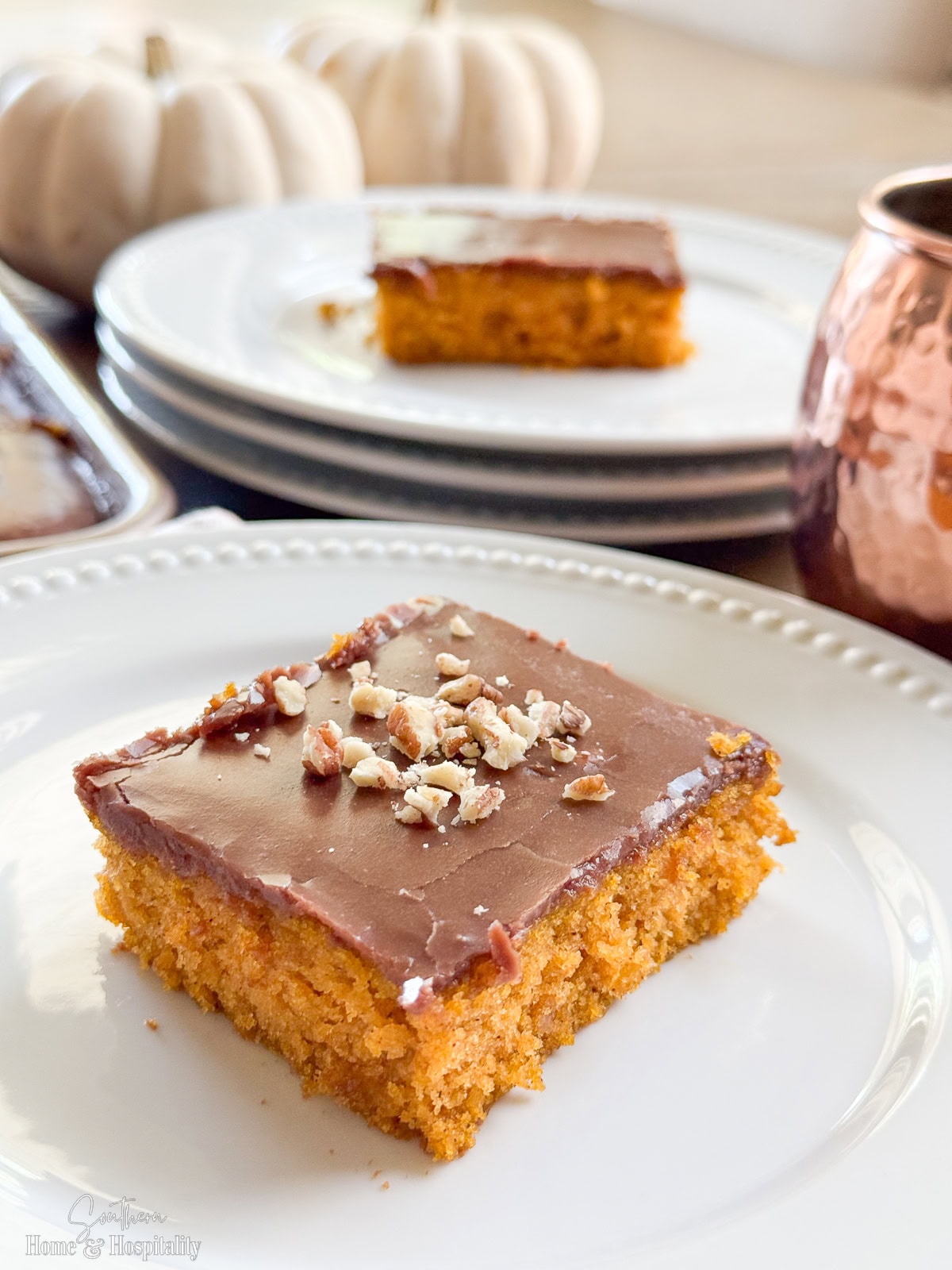 Square of pumpkin spice Texas sheet cake on a white plate with glossy chocolate icing and pecan pieces.