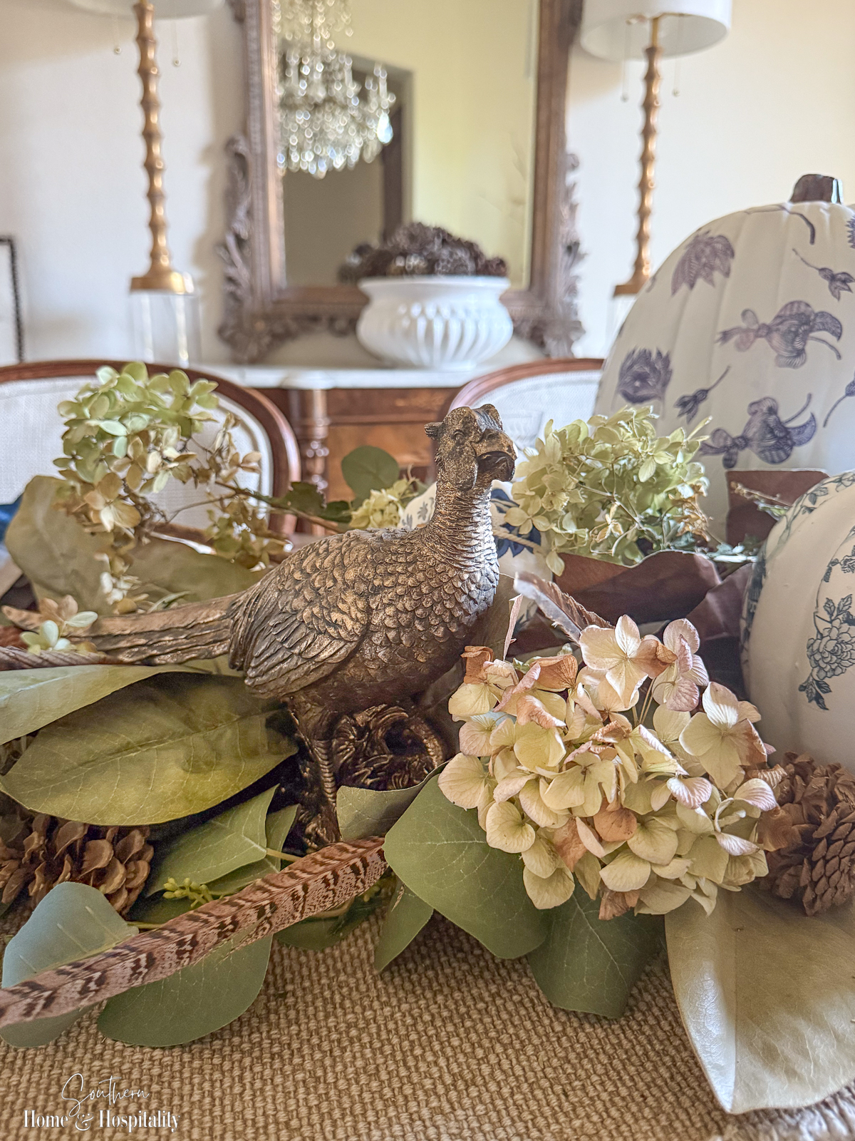 Magnolia leaves and blue and white chinoiserie pumpkins in a fall table centerpiece with eucalyptus, hydrangeas, and a brass pheasant