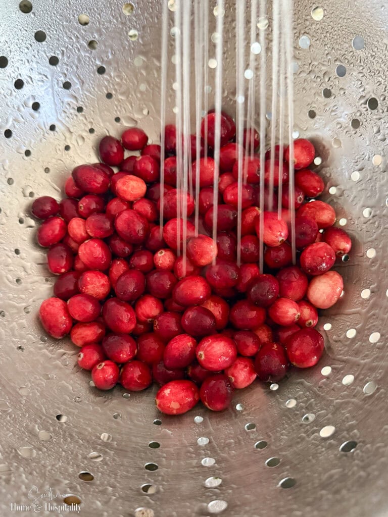 Fresh cranberries being rinsed in a colander before making homemade cranberry sauce.