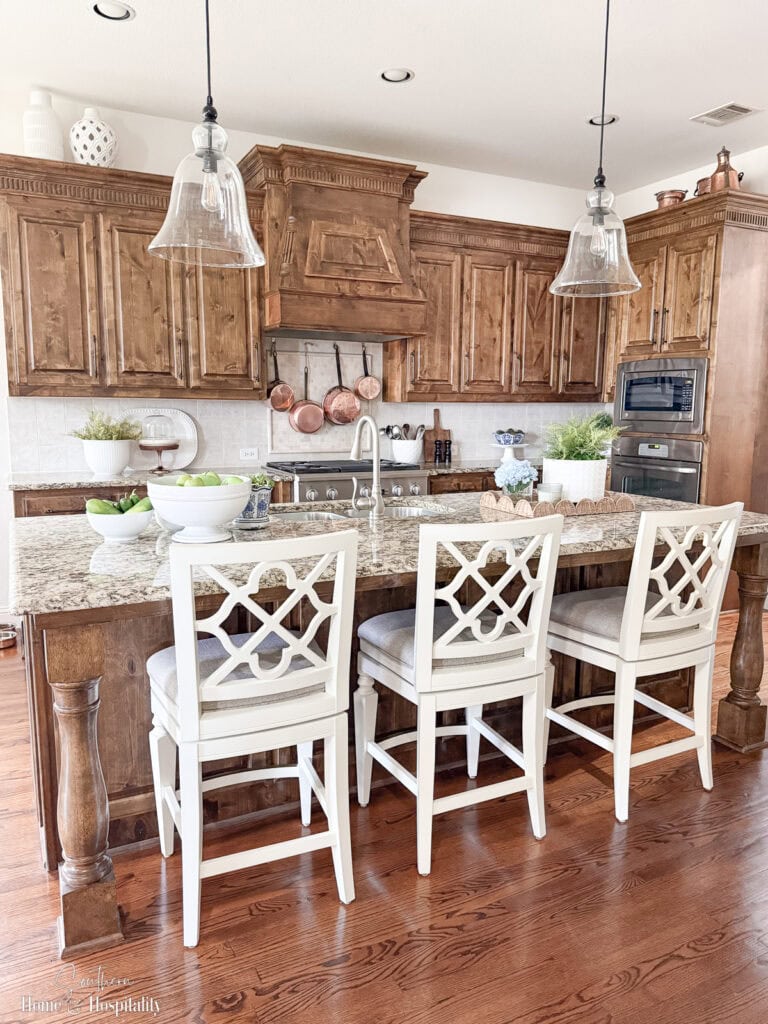 Kitchen with upper cabinets that stop short of ceiling and minimal decor above—white pottery, copper, and glass groupings spaced apart for balanced look