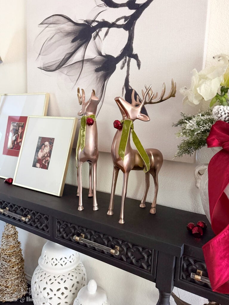 Framed Santa photos and metallic reindeer with red and green accents on console table.