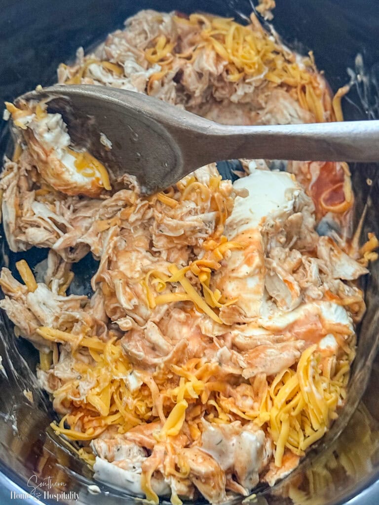 Buffalo chicken dip partially stirred in a slow cooker while the cream cheese melts