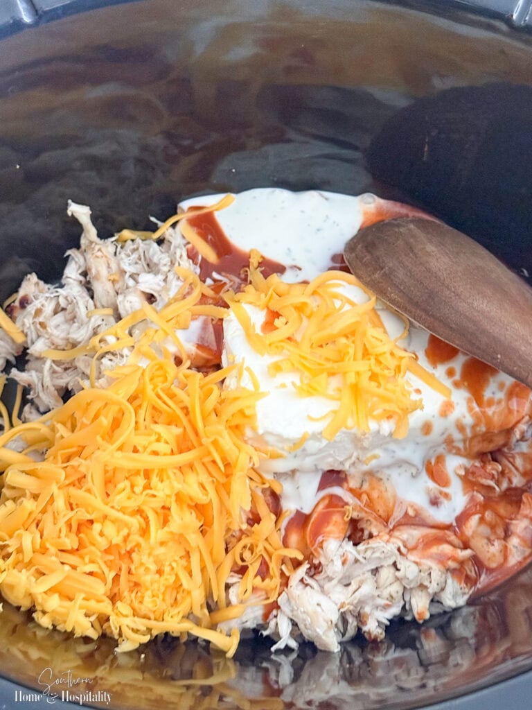 Buffalo chicken dip ingredients added to a slow cooker before stirring