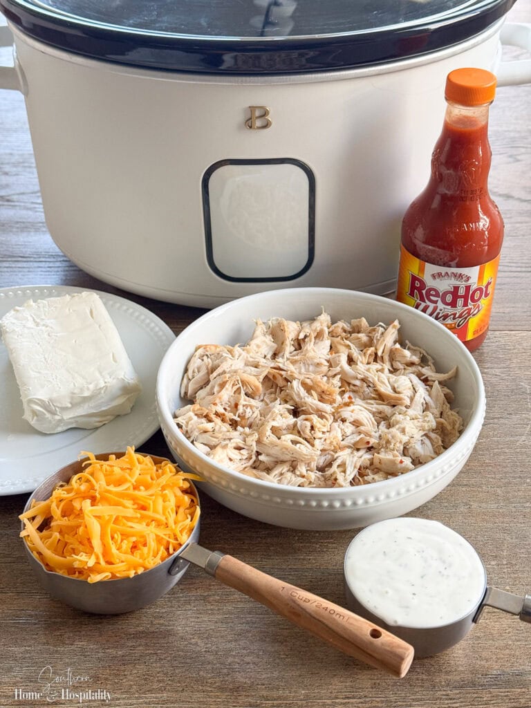 Ingredients for buffalo chicken dip including shredded chicken, cream cheese, cheddar cheese, ranch dressing, and buffalo wing sauce