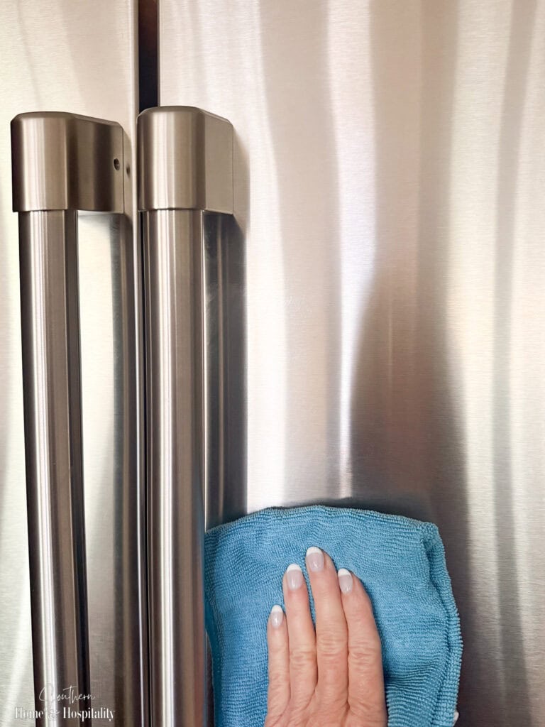 Wiping a stainless steel refrigerator with a microfiber cloth following the grain to prevent streaks.