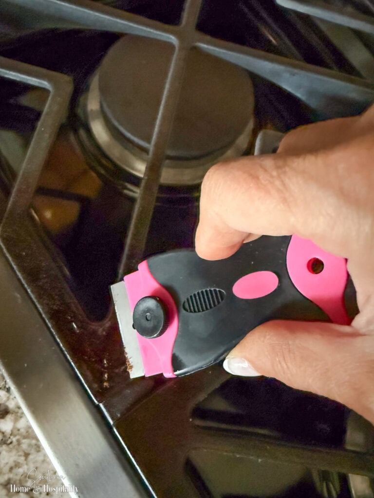 Using a razor scraper to remove burnt-on food from a cooktop surface.