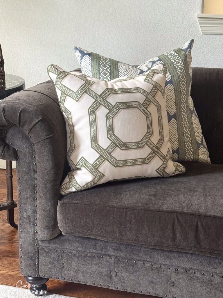 Layered throw pillows in mixed patterns arranged on a gray sofa to show contrast and scale.