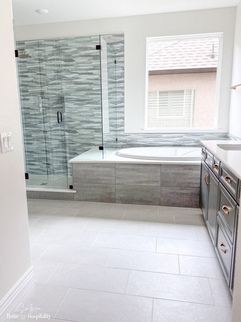 Primary bathroom with statement shower tile, gray vanity, brass hardware, and neutral flooring