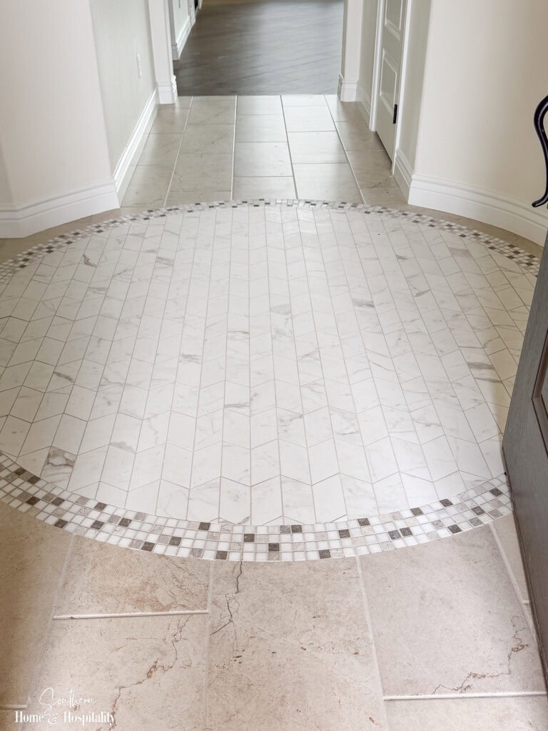 Neutral wood flooring transitioning from a tiled foyer with mosaic into the main living area of a new home