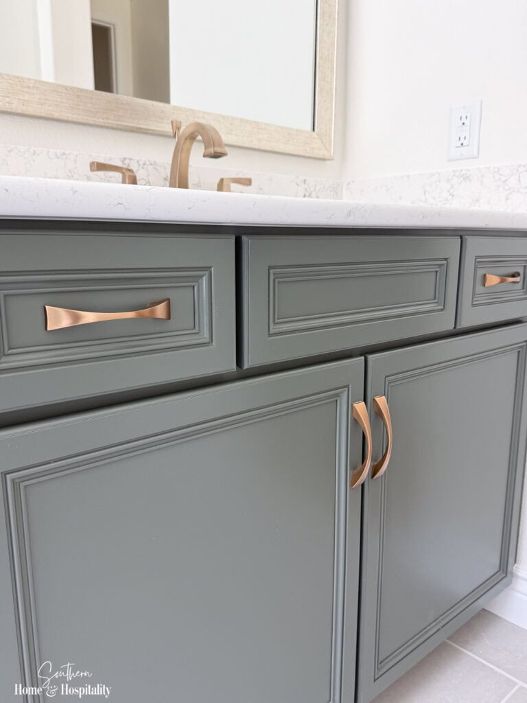 Soft gray-green bathroom vanity with champagne brass hardware and quartz countertop