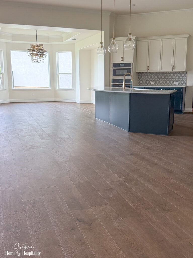 Open-concept kitchen with blue island, warm wood floors, white cabinets, and brass accents