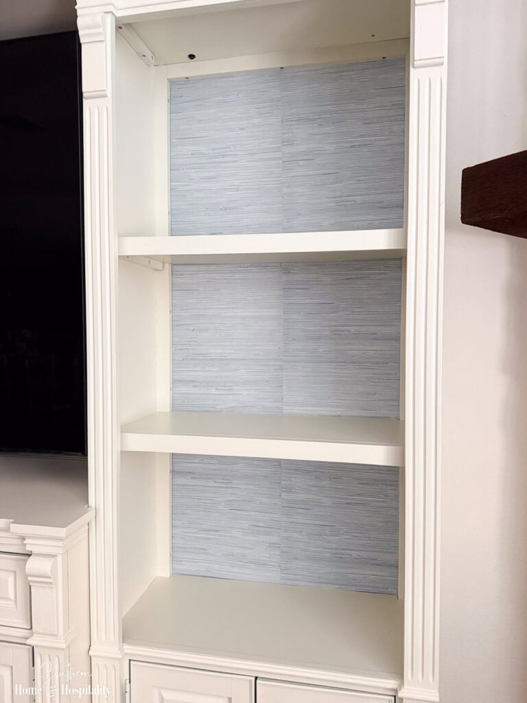 Bookshelf back covered with peel-and-stick wallpaper showing the centered seam before styling the shelves.