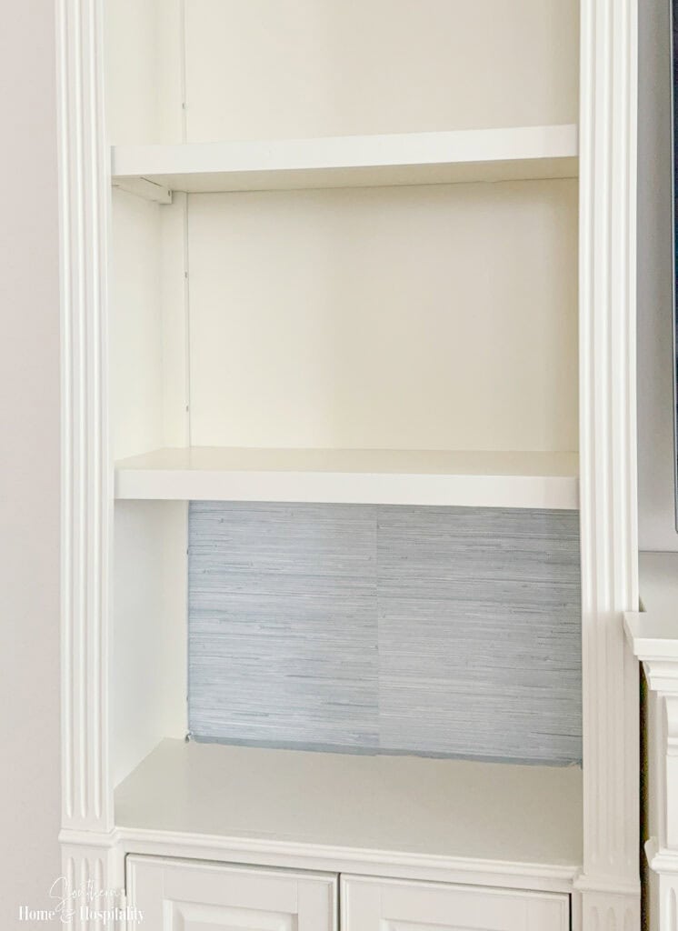 Peel-and-stick wallpaper installed on a bookshelf back with excess material left for trimming around the edges.