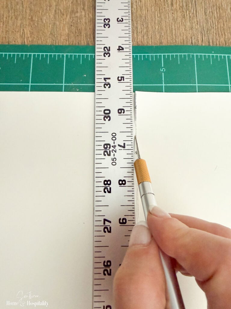 Cutting peel-and-stick wallpaper with a metal ruler and X-Acto knife before installing it on bookshelf backs.