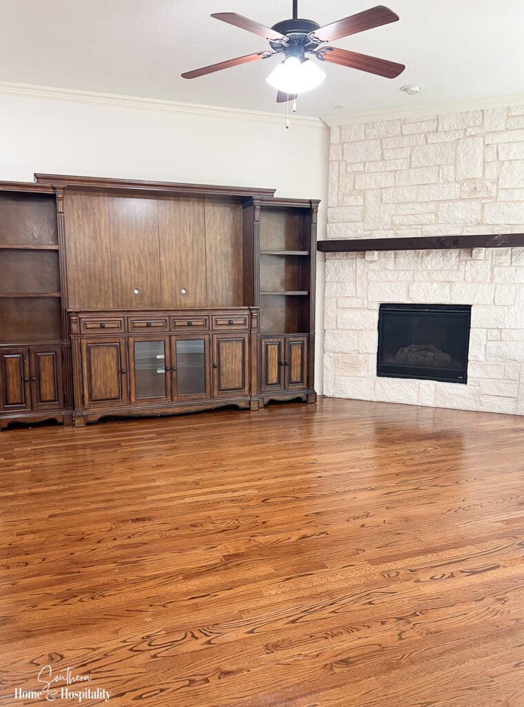 Original dark brown entertainment center left with the house before painting, hardware updates, and peel-and-stick wallpaper were added to the shelves.