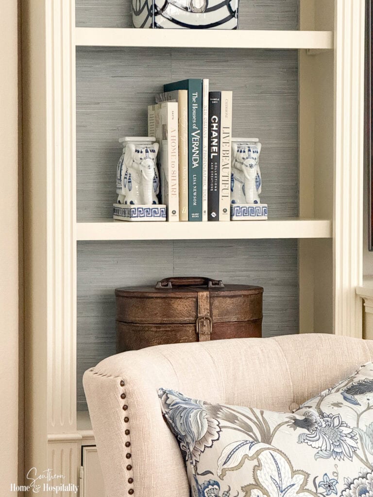 Books, elephant bookends, and decorative accessories displayed against faux grasscloth wallpaper on bookshelf backs.