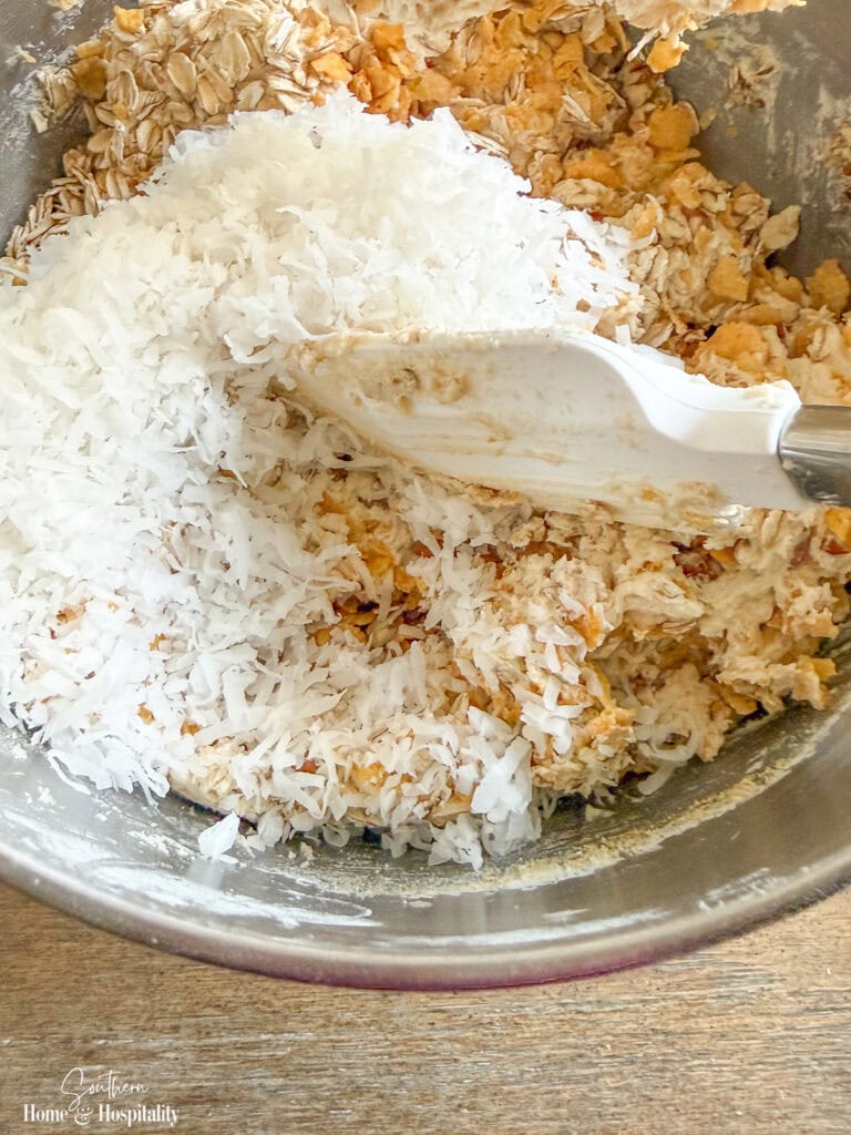 Sweetened flaked coconut being added to Ranger Cookie dough.