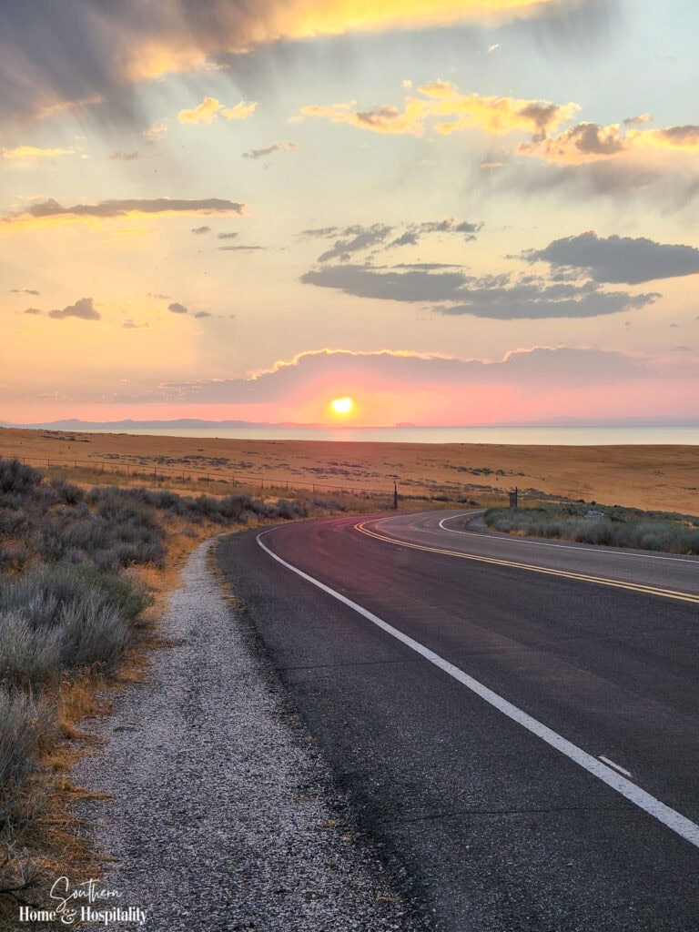 Scenic two-lane highway winding through the red rock desert landscape of southern Utah at sunset.