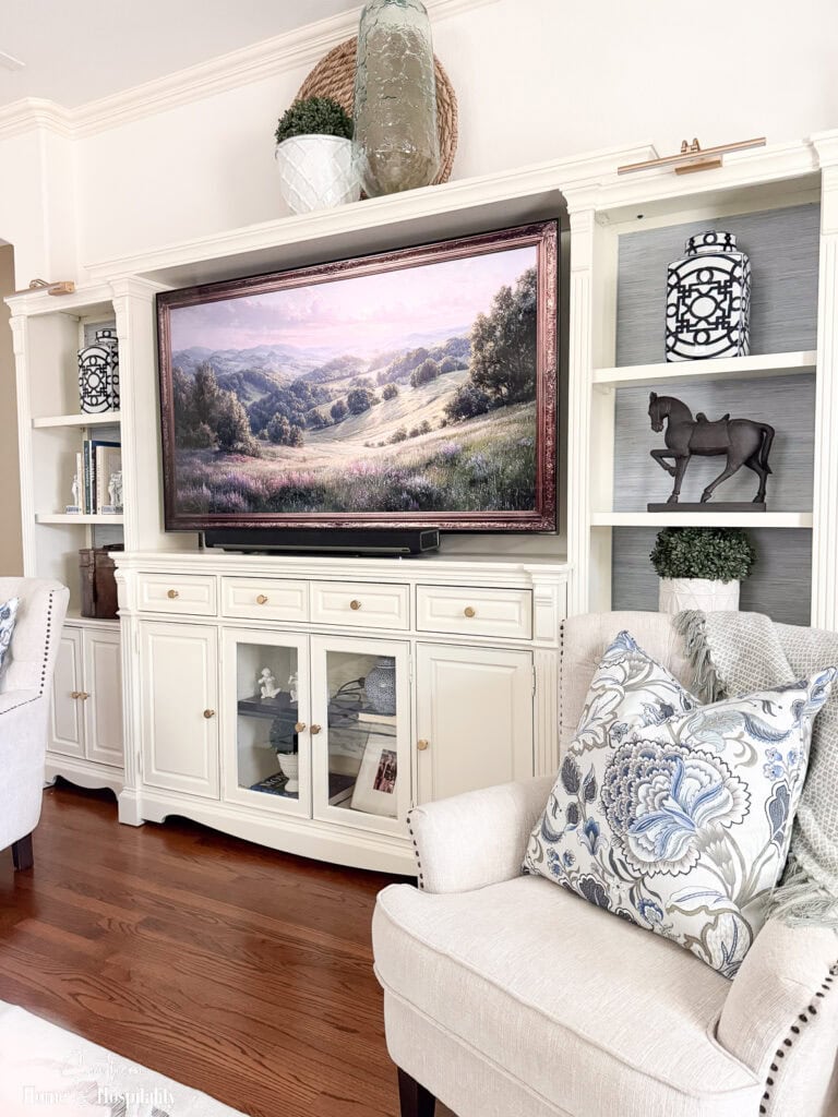 Side view of the updated entertainment center showing wallpaper, accessories, and layered shelf styling with chairs in front.