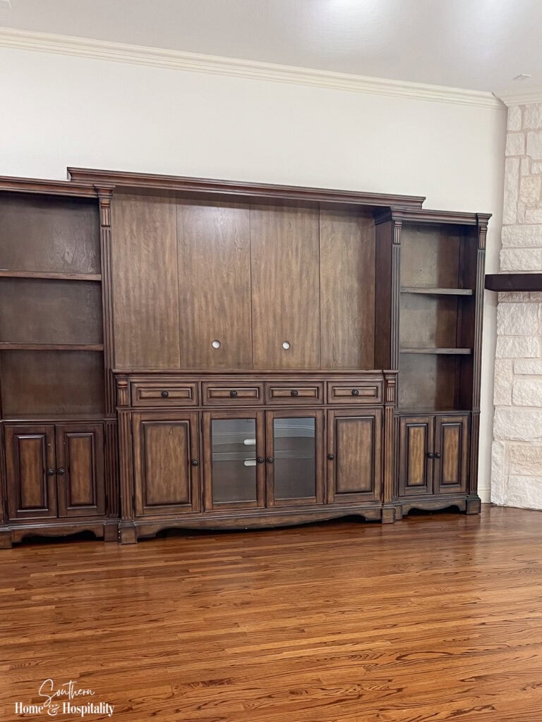 Dark stained entertainment center with glass cabinet doors before being updated.